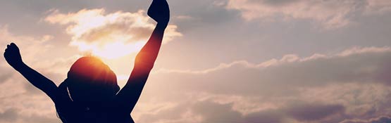 Woman raising hands at sunrise